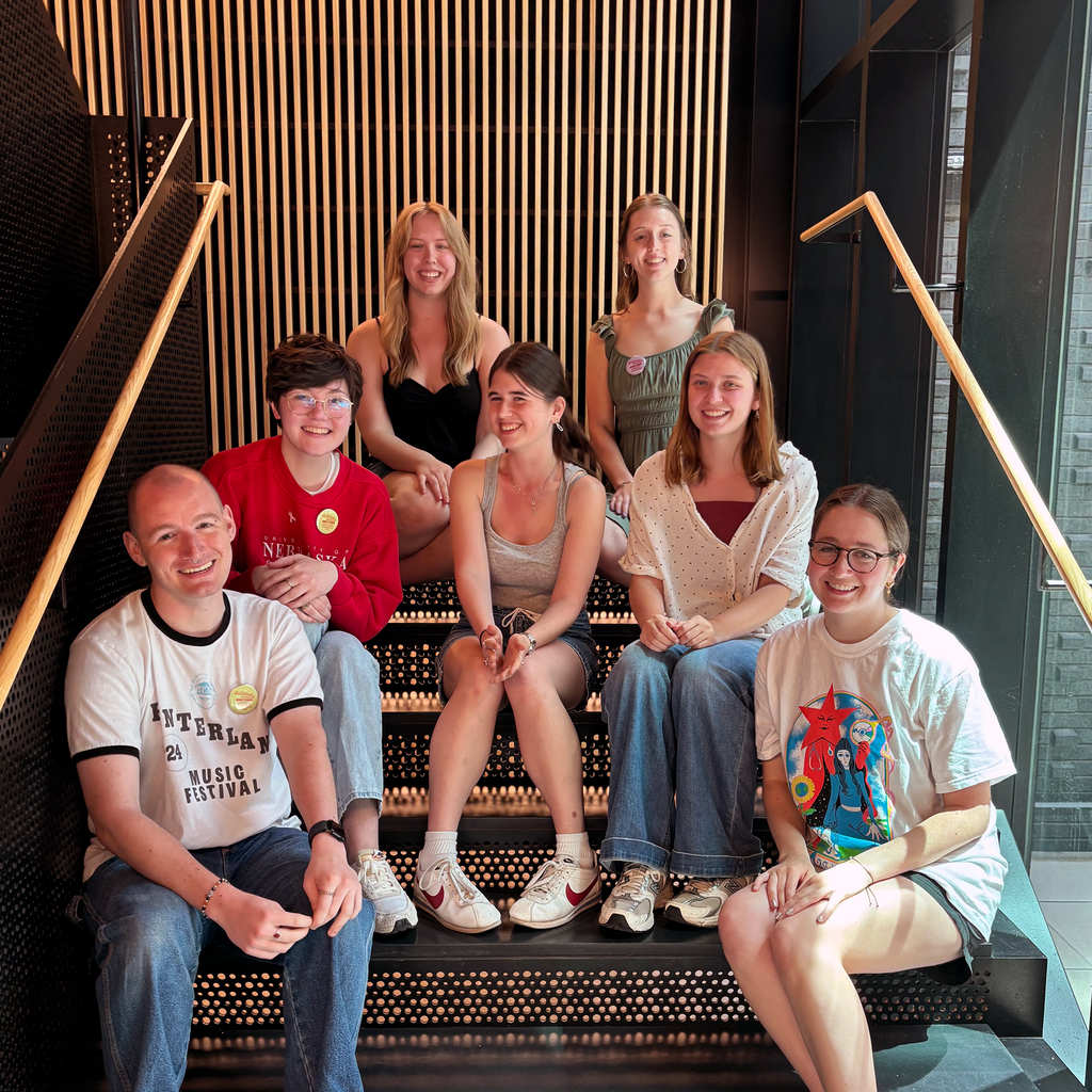 Seven graduating senior student employees sit on the stairs at the Stanley Museum of Art.