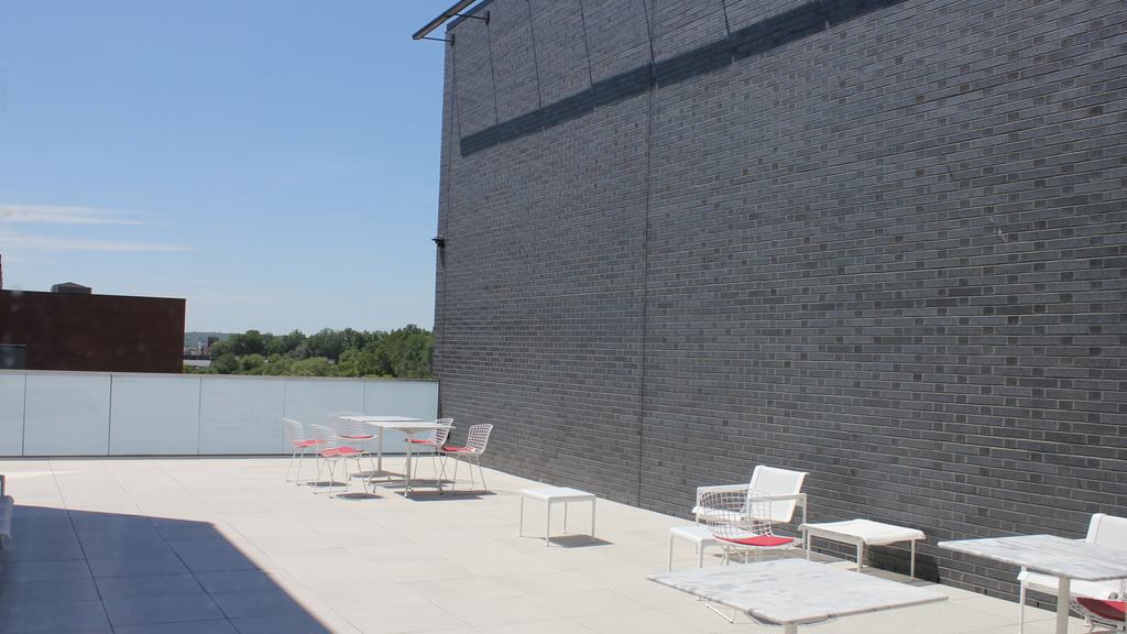 A wide terrace with white chairs and tables overlooks surrounding buildings.